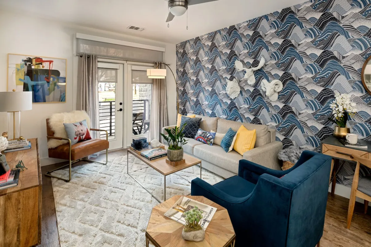 A cozy seating area featuring a comfortable sofa with colorful cushions, a stylish accent chair, and a decorative coffee table set against textured wave-patterned wallpaper. Soft lighting and serene decor create a welcoming and intimate atmosphere, ideal for relaxing during a romantic getaway or solo retreat.