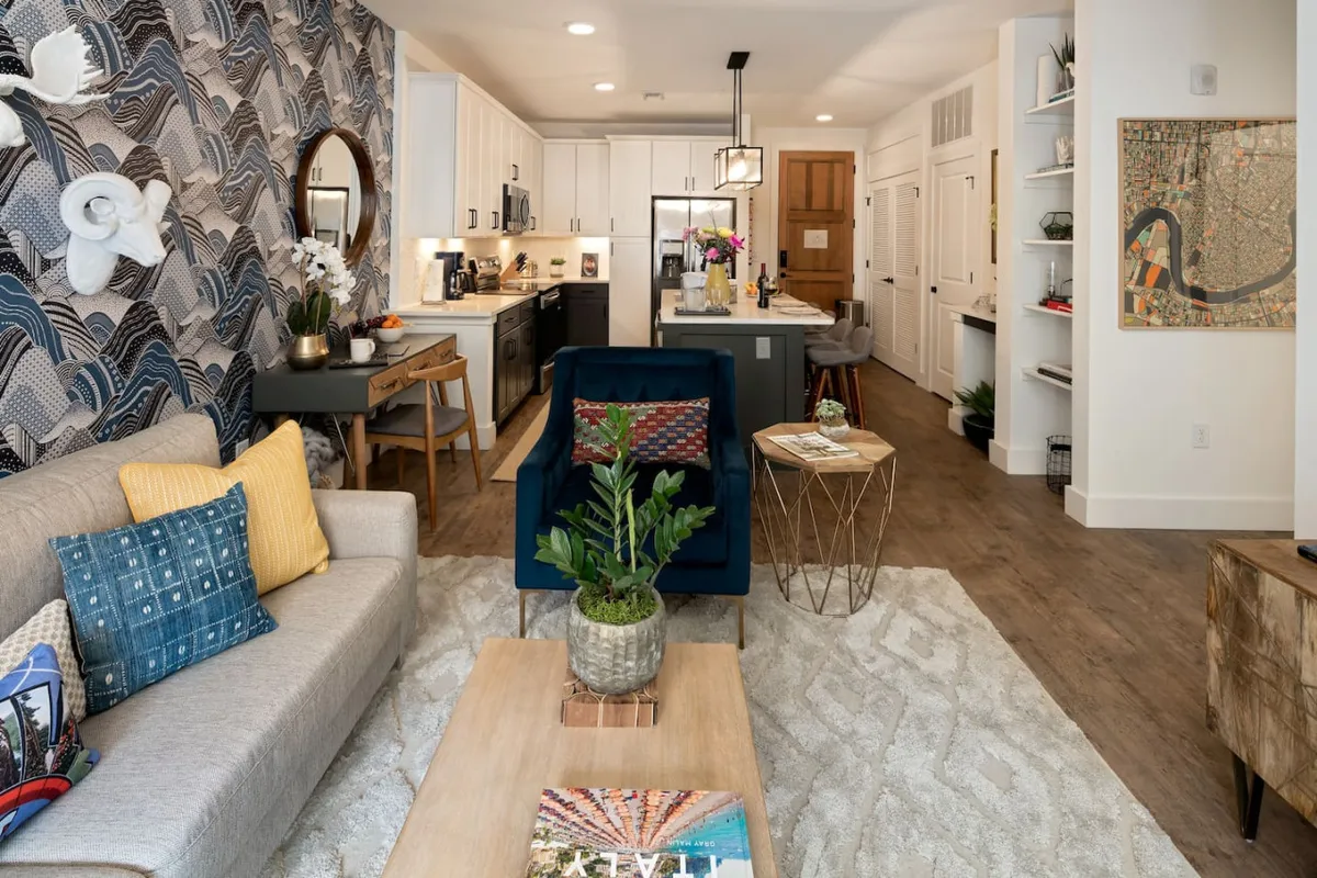 A welcoming living and dining space with a sofa adorned with colorful pillows, a blue armchair, a dining table set with decorative items, and vibrant wall art. The arrangement encourages both relaxation and social gatherings.
