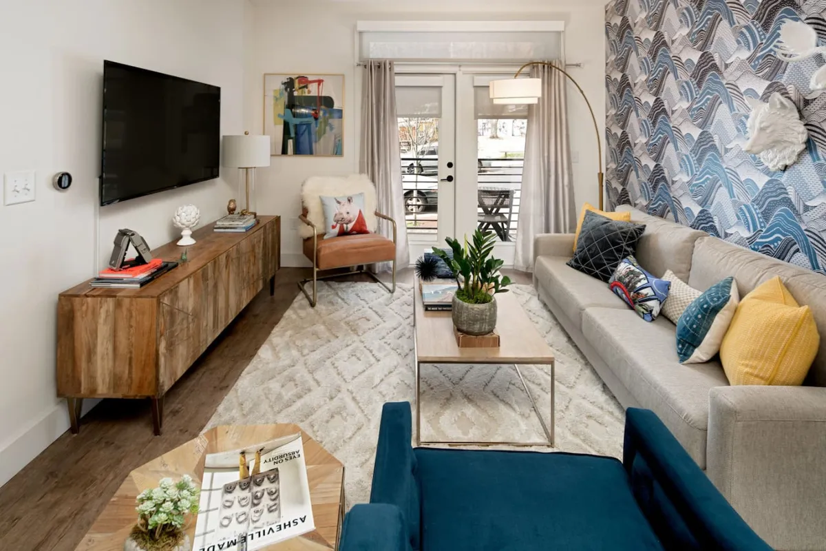 A bright, inviting living area features a plush sofa adorned with colorful cushions, a warm wooden coffee table, striking wall art, and a sleek TV unit, all set within an open-concept layout that feels both stylish and comfortable.