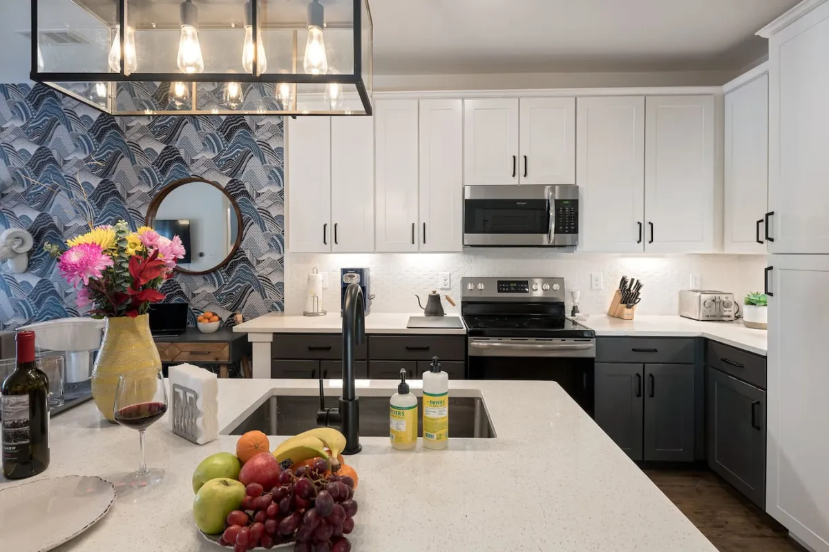 The kitchen island is the focal point here, adorned with a vibrant flower arrangement and a bowl of fresh fruit. Open shelving displays kitchenware, reinforcing the fully equipped nature of the space. The atmosphere is bright and lively, ideal for casual dining or prepping meals.