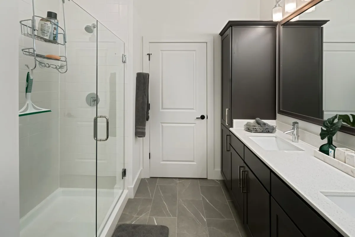 A modern bathroom with a glass shower enclosure, double sink vanity with a large mirror, and dark cabinetry. The space is designed for personal grooming and relaxation, embodying spa-like comfort and sophistication.